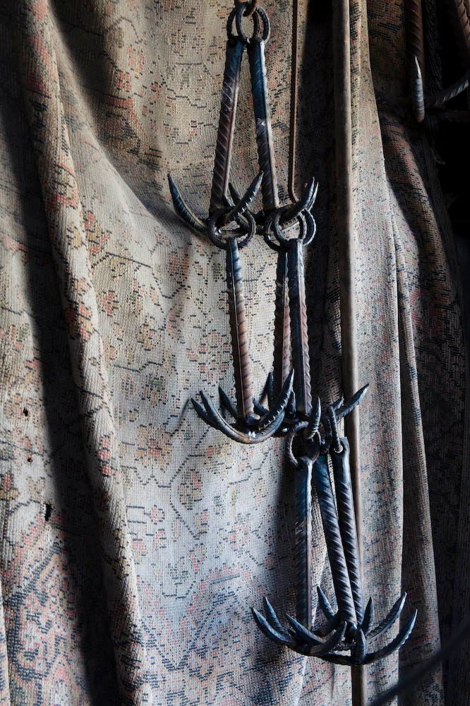 Three hand-forged iron hooks hanging against a faded, patterned curtain.