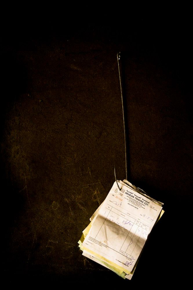 A stack of old handwritten invoices hanging from a single hook against a dark background.